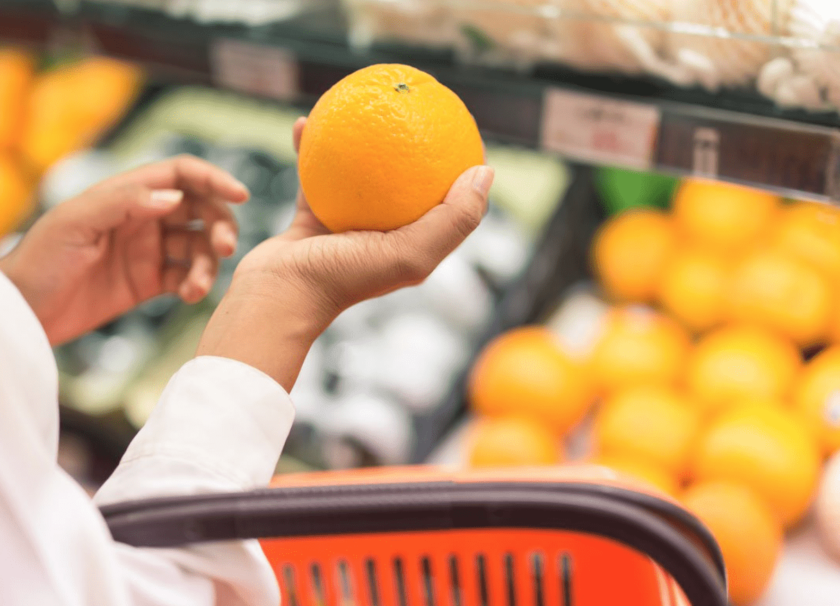 Una mano femenina cogiendo una naranja en el supermercado.
